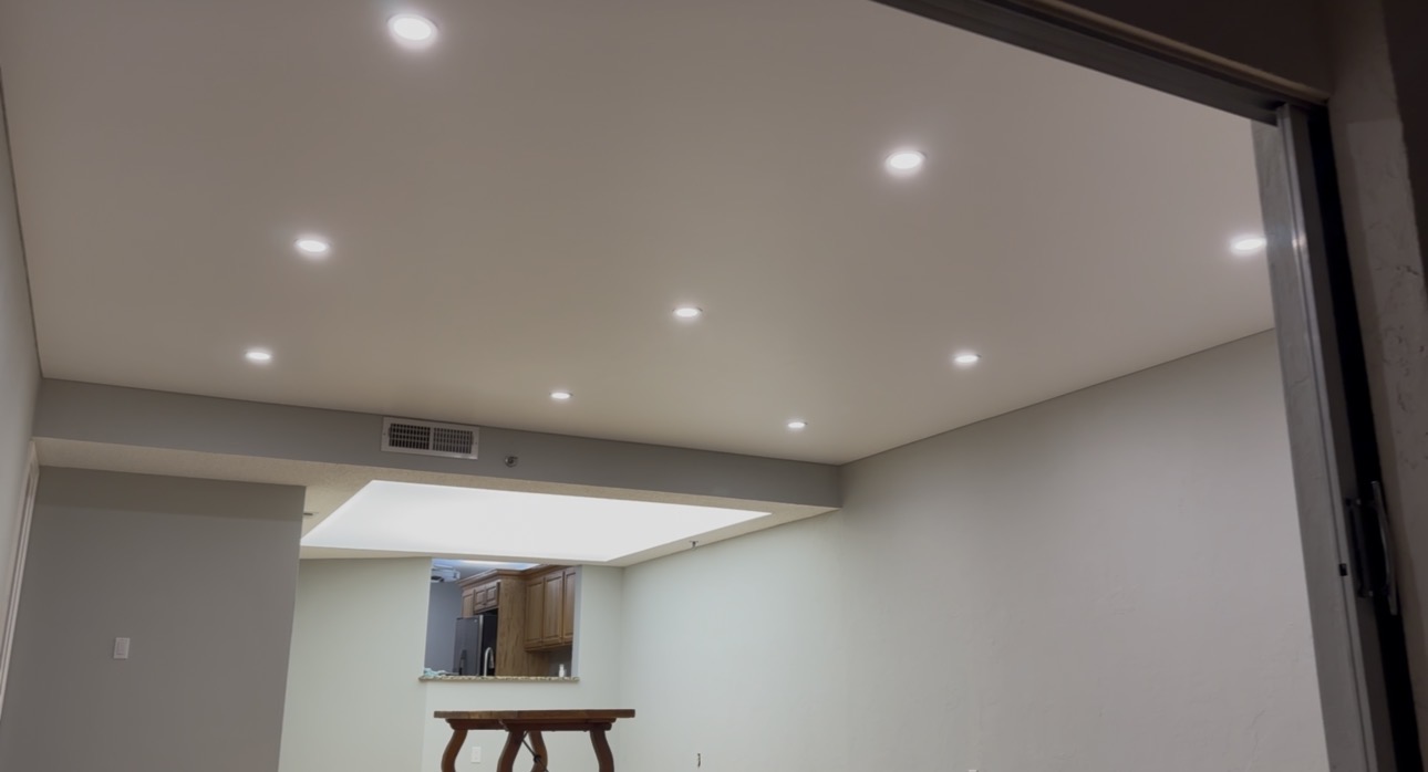 Matte white stretch ceiling with 9 recessed LED puck lights in residential space