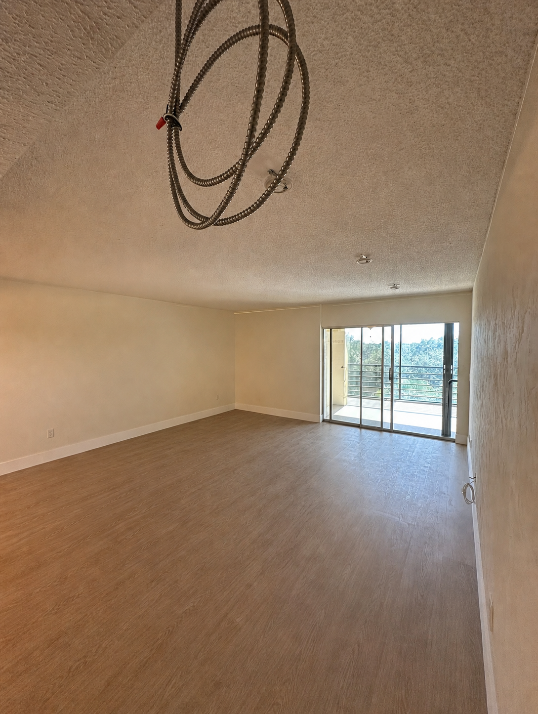 Living room before installation showing exposed concrete ceiling with popcorn texture and hanging wiring